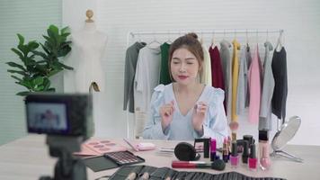 blogueira de beleza apresenta cosméticos de beleza sentados na frente da câmera para gravar vídeo. linda mulher asiática usa escova enquanto revisão tutorial de maquiagem transmitido vídeo ao vivo para rede social pela internet. video