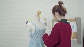 Diseñador de moda femenina asiática hermosa profesional trabajando vestido de medición en un diseño de ropa de maniquí en el estudio. concepto de trabajo de las mujeres de estilo de vida. video