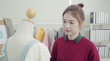 profissional lindo estilista feminino asiático trabalhando medindo vestido em um design de roupas de manequim no estúdio. conceito de trabalho das mulheres do estilo de vida. video