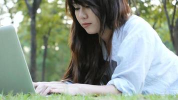 benen van de jonge Aziatische vrouw op het groene gras met geopende laptop. video
