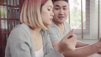 Atractiva pareja asiática joven distraída en la mesa con el periódico y el teléfono celular mientras desayuna. video