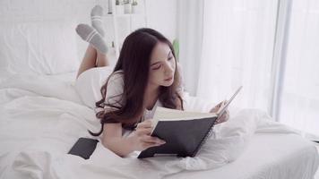 Portrait of beautiful attractive Asian woman reading a book while lying on the bed when relax in her bedroom at home. video