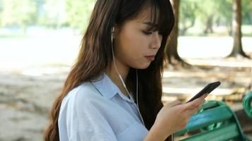 Mulher bonita está lendo mensagem de texto agradável no celular enquanto está sentada no parque em um dia quente de primavera video