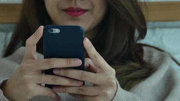 las mujeres asiáticas felices están usando teléfonos inteligentes en la cama por la mañana. video