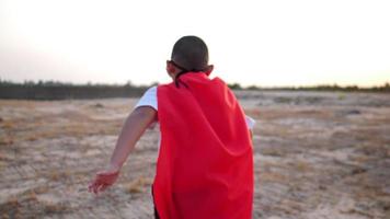 silhueta de um menino se divertindo vestido como um super-herói correndo em um campo video