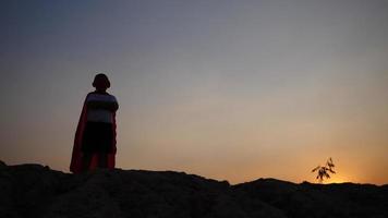 Silhouette of a boy having fun dressed as a superhero running in a field video