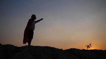 silhouet van een jongen met plezier verkleed als een superheld die in een veld loopt video