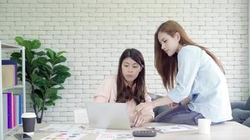aantrekkelijke slimme creatieve Aziatische zakenvrouwen in slimme vrijetijdskleding die aan laptop werken terwijl ze op het bureau op het bureau zitten. video