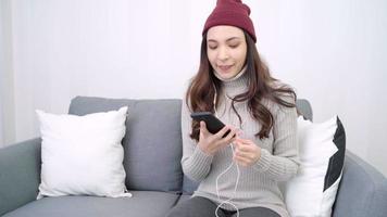 Asian woman uses smartphone for texting, reading, messaging and buying online while lying on home sofa in her living room at home.  video