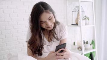 cámara lenta - hermosa mujer asiática con smartphone mientras está acostado en la cama en su dormitorio. video