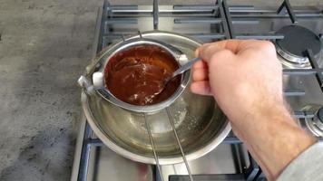 Vista de templado de chocolate derretido en una olla de baño maría. Vertido y mezcla de granos de cacao procesados licuados video