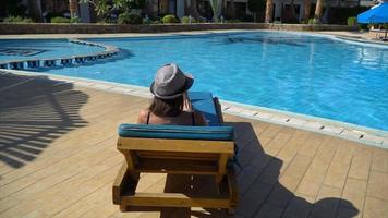 Femme mince insouciante se détend et prend un bain de soleil près de la piscine en une journée d'été video