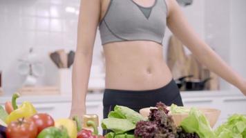 giovane donna asiatica che fa insalata cibo sano durante l'utilizzo di tablet per cercare ricetta in cucina. video