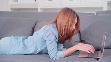 mujer asiática con computadora o computadora portátil mientras está acostado en el sofá. video