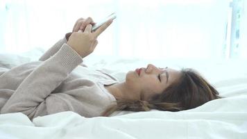 las mujeres asiáticas felices están usando teléfonos inteligentes en la cama por la mañana. video