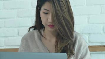 mooie jonge lachende Aziatische vrouw die op laptop werkt zittend op bed in de slaapkamer thuis. video