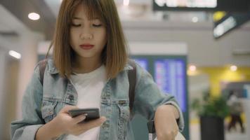 gelukkige Aziatische vrouw die haar smartphone in terminalzaal gebruikt en controleert.