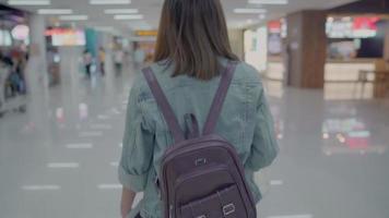 Feliz mujer asiática con carro o carro con muchos equipajes caminando en el hall de la terminal. video