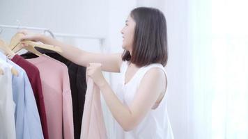 joven asiática eligiendo su traje de moda en casa o tienda. video