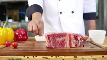 Nahaufnahme des Gourmetkochs oder des Kochs, der ein frisches Stück Rindfleisch mit Meersalz und gemahlenen würzigen Paprikaschoten würzt. video