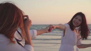 jovens amigos asiáticos usando uma câmera, tirando fotos uns dos outros na praia. video