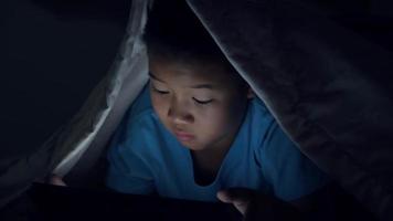 Niño usando tableta debajo de la manta por la noche en la cama video
