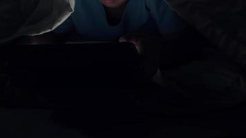 Little boy using tablet under blanket at night in bed video