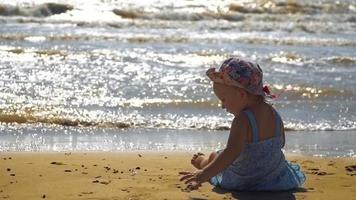 liten flicka som sitter på sanden vid havet video