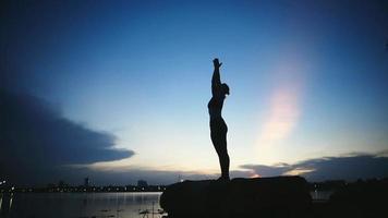 siluettvideokvinna som gör yoga vid sjön i parken