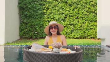 Joven mujer asiática disfrutando de un desayuno flotante en la piscina video