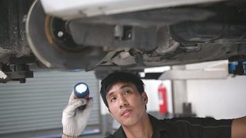 Asian mechanical holds a flashlight to examine under the car video