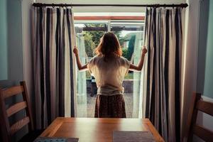 Mujer joven abriendo las cortinas al amanecer.