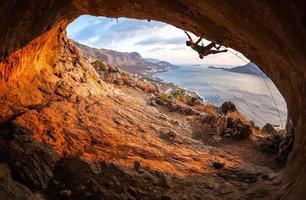Male rock climber climbing along a roof in a cave photo