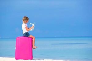 niña sosteniendo un mapa y sentado en el equipaje en una playa