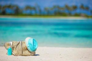 Bolsa de mimbre con sombrero y protector solar en la playa foto