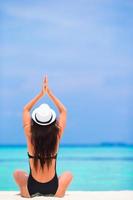 Mujer con sombrero meditando en una playa foto