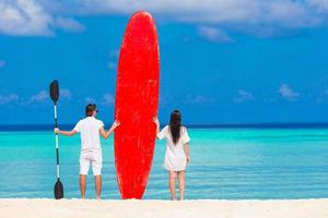 Two people standing on a beach with a paddleboard photo