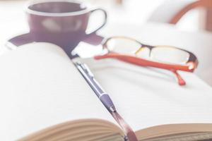 Pen, notebook, coffee cup, and eyeglasses on a wooden table photo