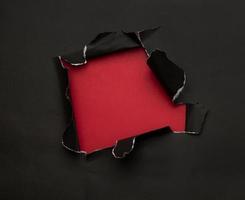 Black torn paper on red background photo