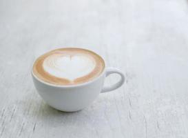 Cup of latte with heart shape on white table photo