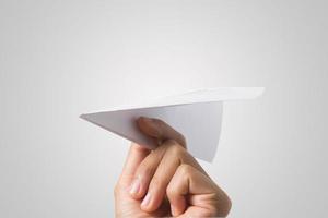 La mano de una mujer sostiene un avión de papel sobre fondo blanco. foto