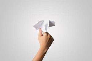 La mano de una mujer sostiene un avión de papel sobre fondo blanco. foto