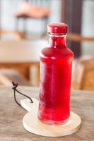 Jarabe rojo en una botella sobre una placa de madera foto