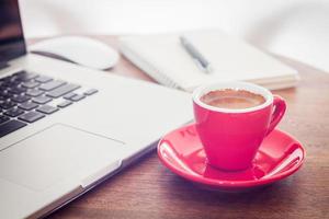 Taza de café roja sobre una mesa con un portátil