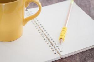 Yellow coffee cup and pencil on a notebook photo