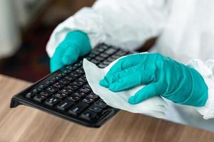 Person with protective equipment cleaning a computer keyboard photo