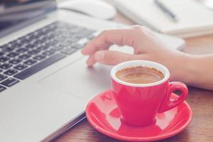 taza de café roja y una persona en una computadora portátil foto