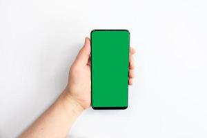 Mujer sosteniendo un teléfono móvil de pantalla verde con un fondo blanco. foto