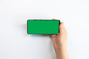 Mujer sosteniendo un teléfono móvil de pantalla verde con un fondo blanco.