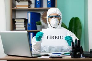 Person in protective suit working on laptop at office photo